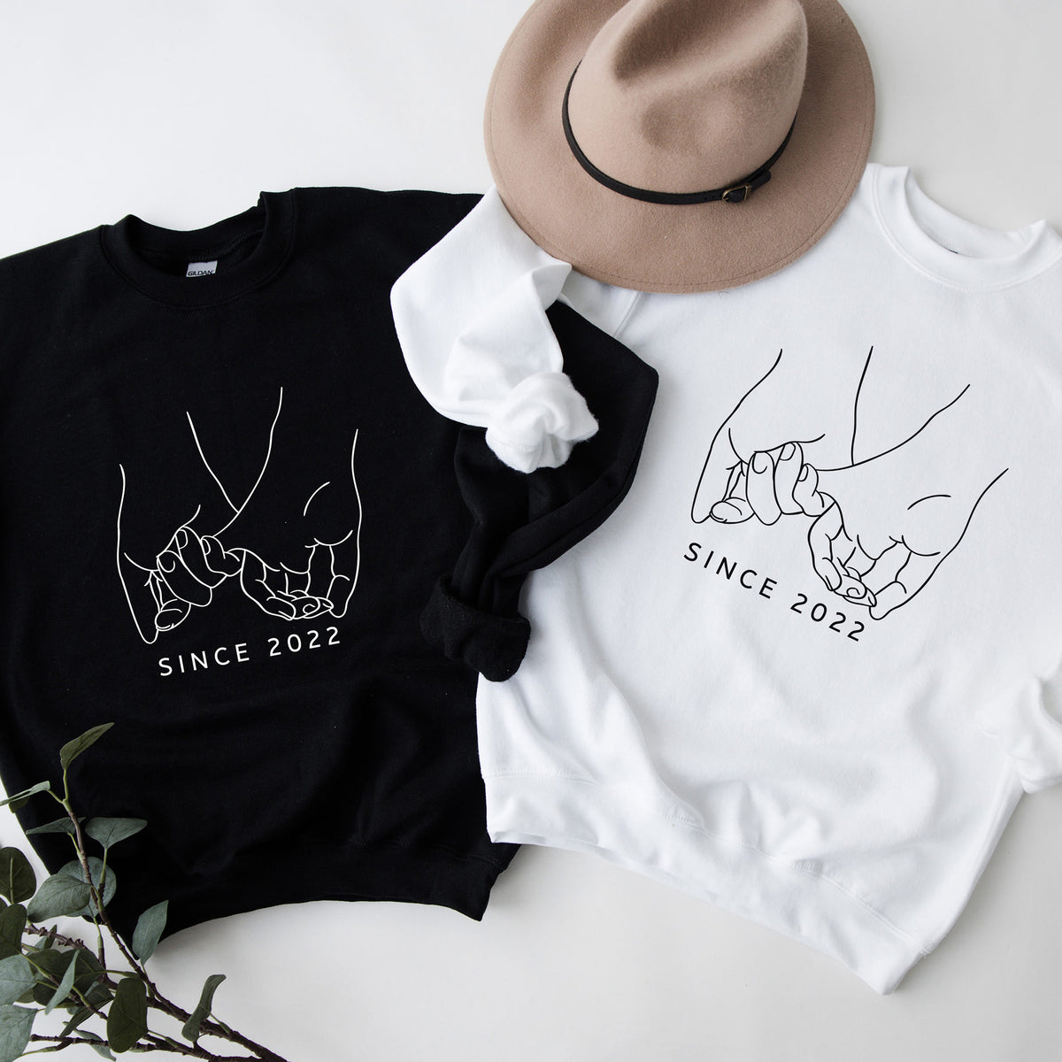 Black and white sweatshirts with 'Since 2022' design and a hat on a light background