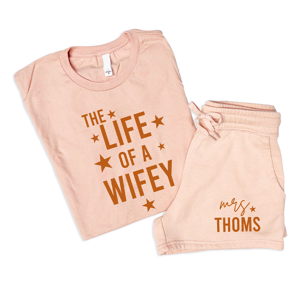 Peach personalized wife summer set with Life of a Wifey t shirt and custom Mrs family name shorts flat lay on white background
