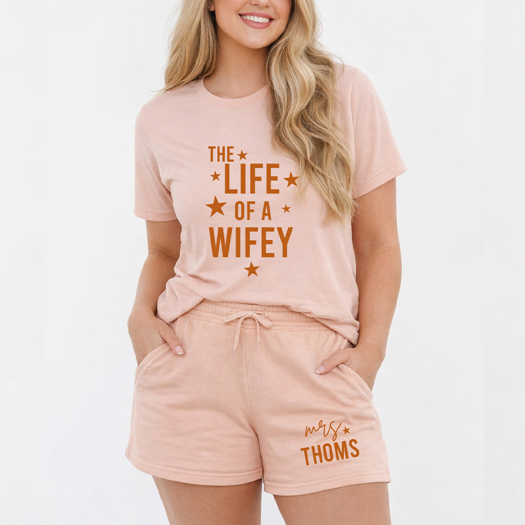 Personalized wife summer set in peach color with Life of a Wifey t shirt and custom Mrs family name shorts worn by female model on white background