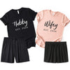 Personalized Hubby and Wifey matching pajama set with black men’s t-shirt, peach women’s t-shirt, and black boxer shorts on white background