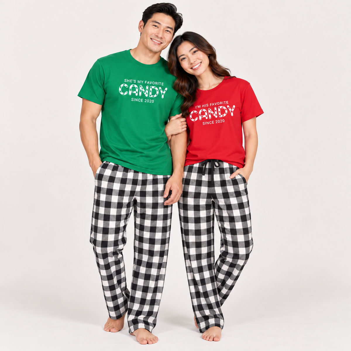 Couple wearing matching favorite candy pajama outfits, featuring Kelly green and red graphic T-shirts with black-and-white buffalo plaid flannel pajama pants in a studio setting.
