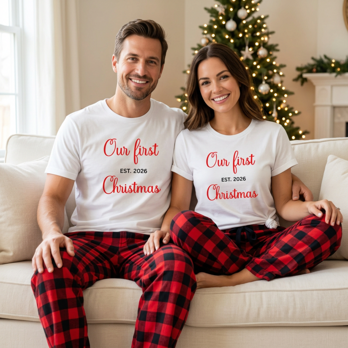 Couple wearing matching Our First Christmas EST. 2026 T-shirts and red-and-black plaid pajama pants beside a Christmas tree.