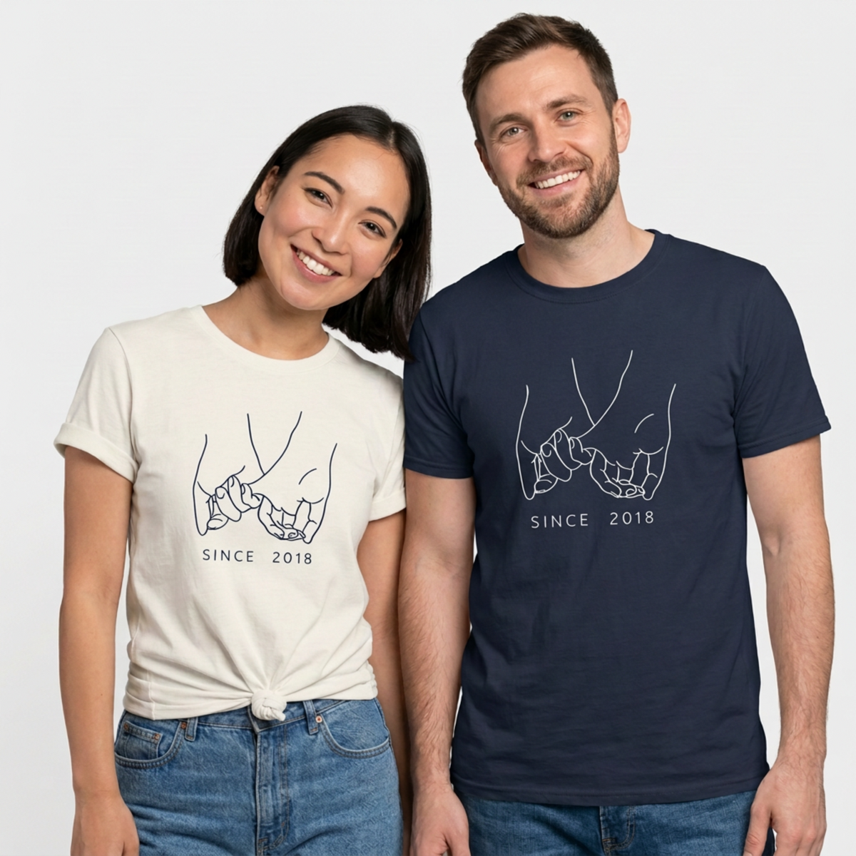 Smiling couple wearing white and navy matching T-shirts with pinky-promise hand illustrations and “Since 2018” text.
