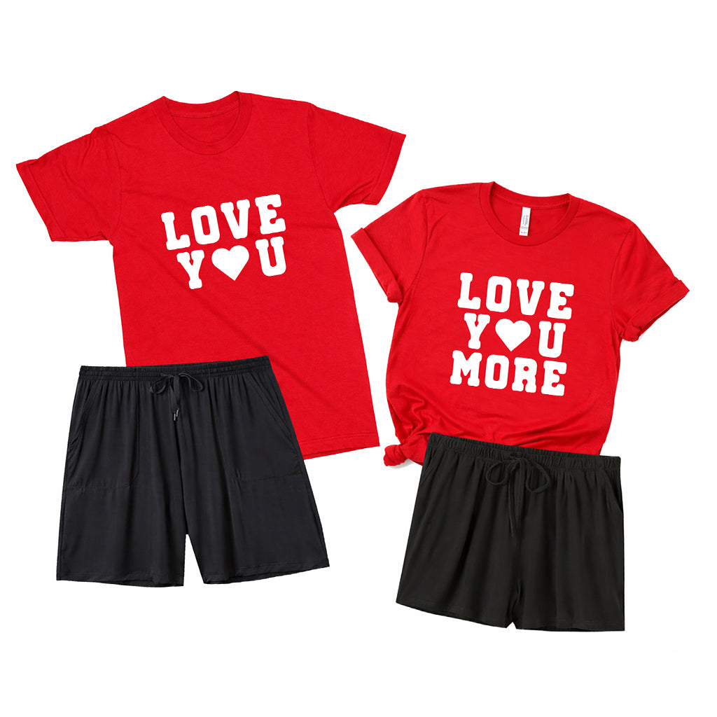 Flat lay of matching couples loungewear set with red “Love You” and “Love You More” t-shirts and black pajama shorts on a white background