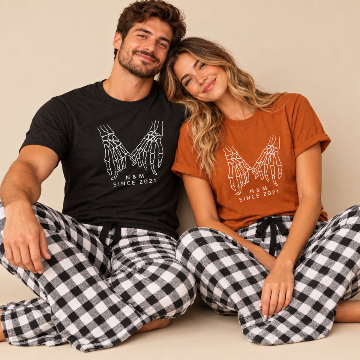 Couple wearing matching skeleton hand holding shirts and black and white plaid pajama pants