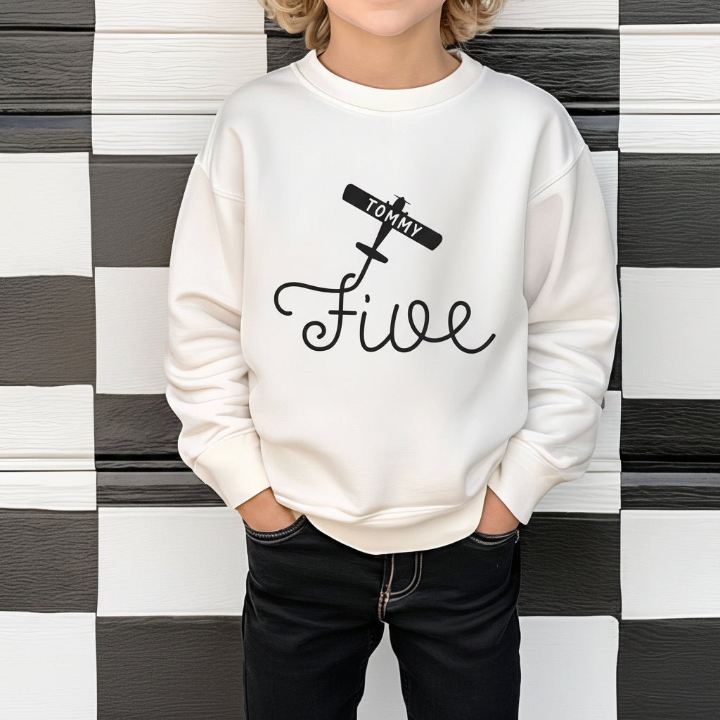 Boy wearing white color personalized 5th birthday airplane sweatshirt against checkered wall background
