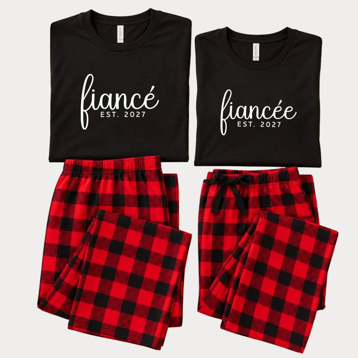 Matching fiancé and fiancée pajama sets featuring long-sleeve jersey tees with “fiancé” and “fiancée” prints and EST. 2027 text, paired with red and black buffalo plaid flannel pajama pants.