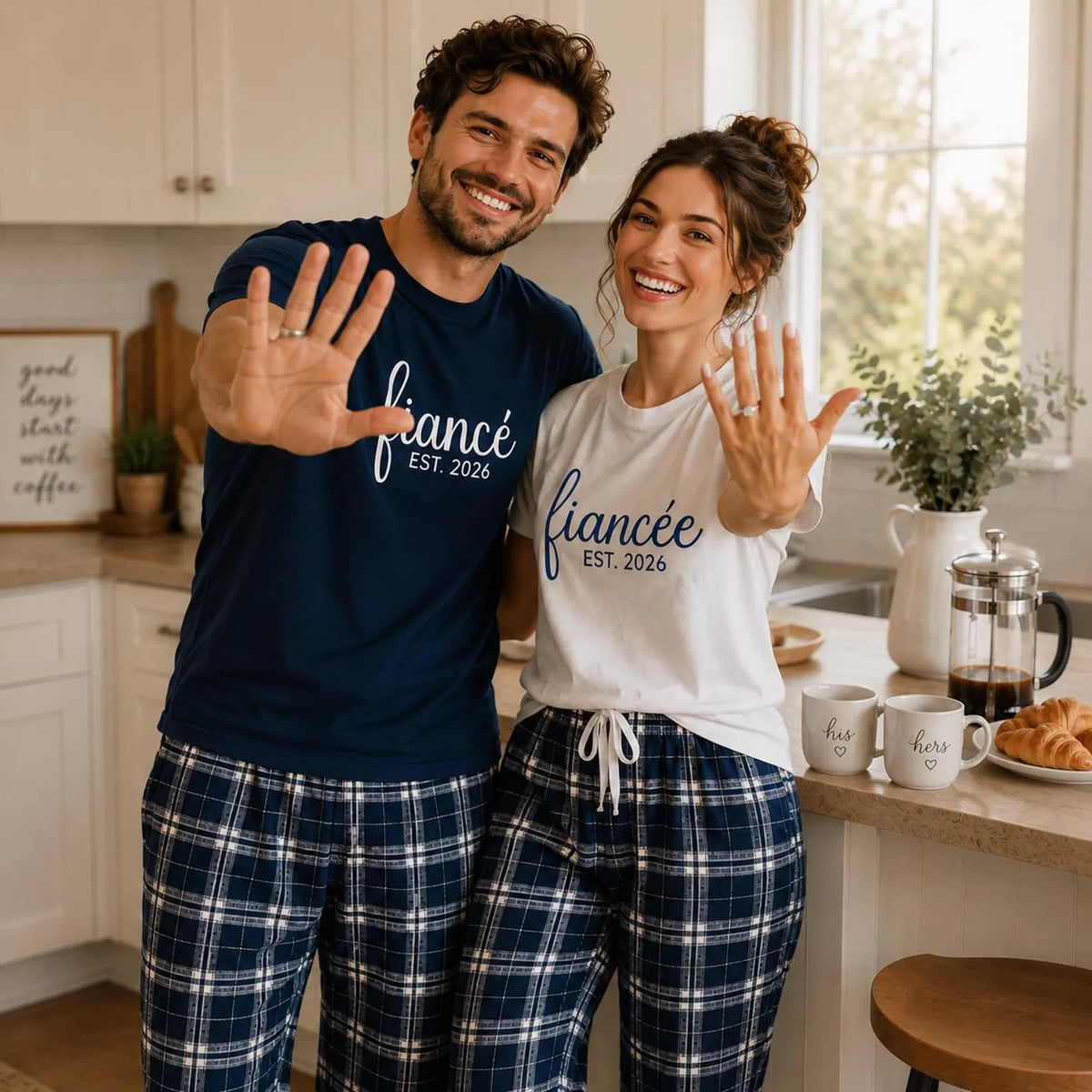 Engaged couple showing their engagement rings while wearing matching fiancé and fiancée unisex T-shirts with navy and silver plaid flannel pajama pants.