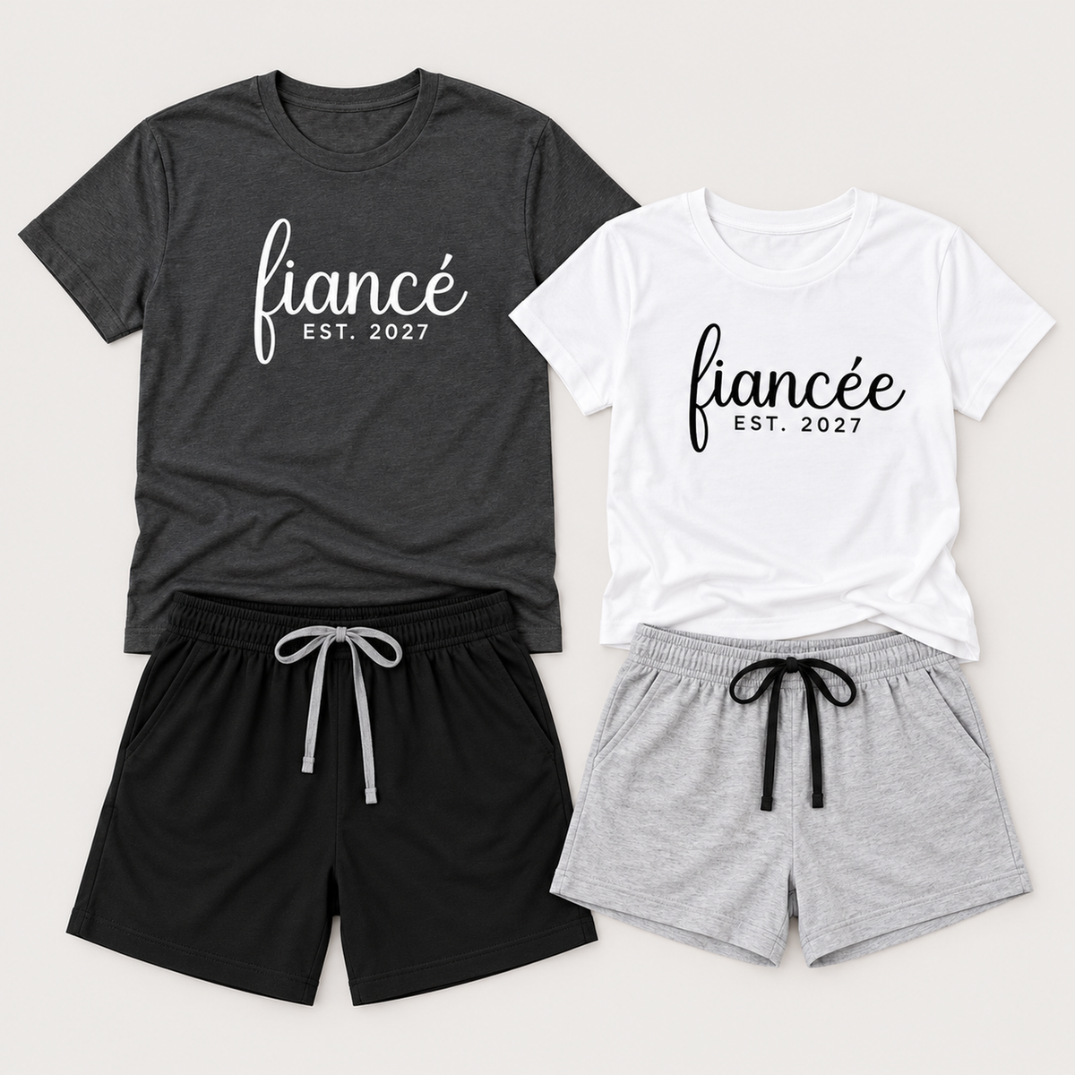 Fiancé and fiancée matching pajama sets arranged flat in a studio, featuring personalized T-shirts with EST. 2027 lettering and coordinating drawstring shorts.