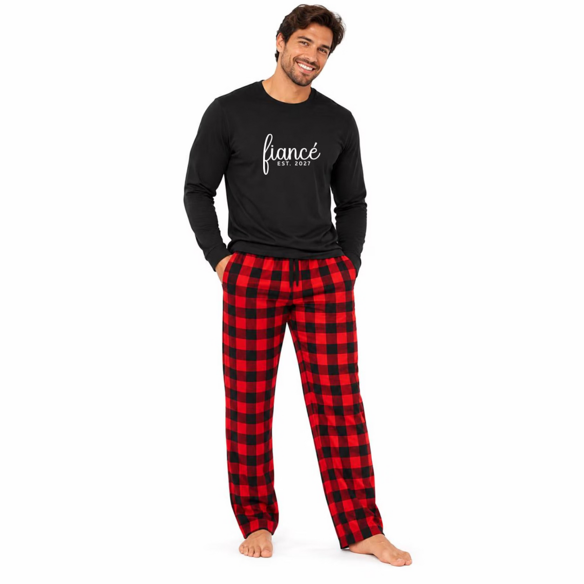 A man wearing a black long-sleeve jersey tee with “fiancé EST. 2027” lettering, paired with red and black buffalo plaid flannel pajama pants.