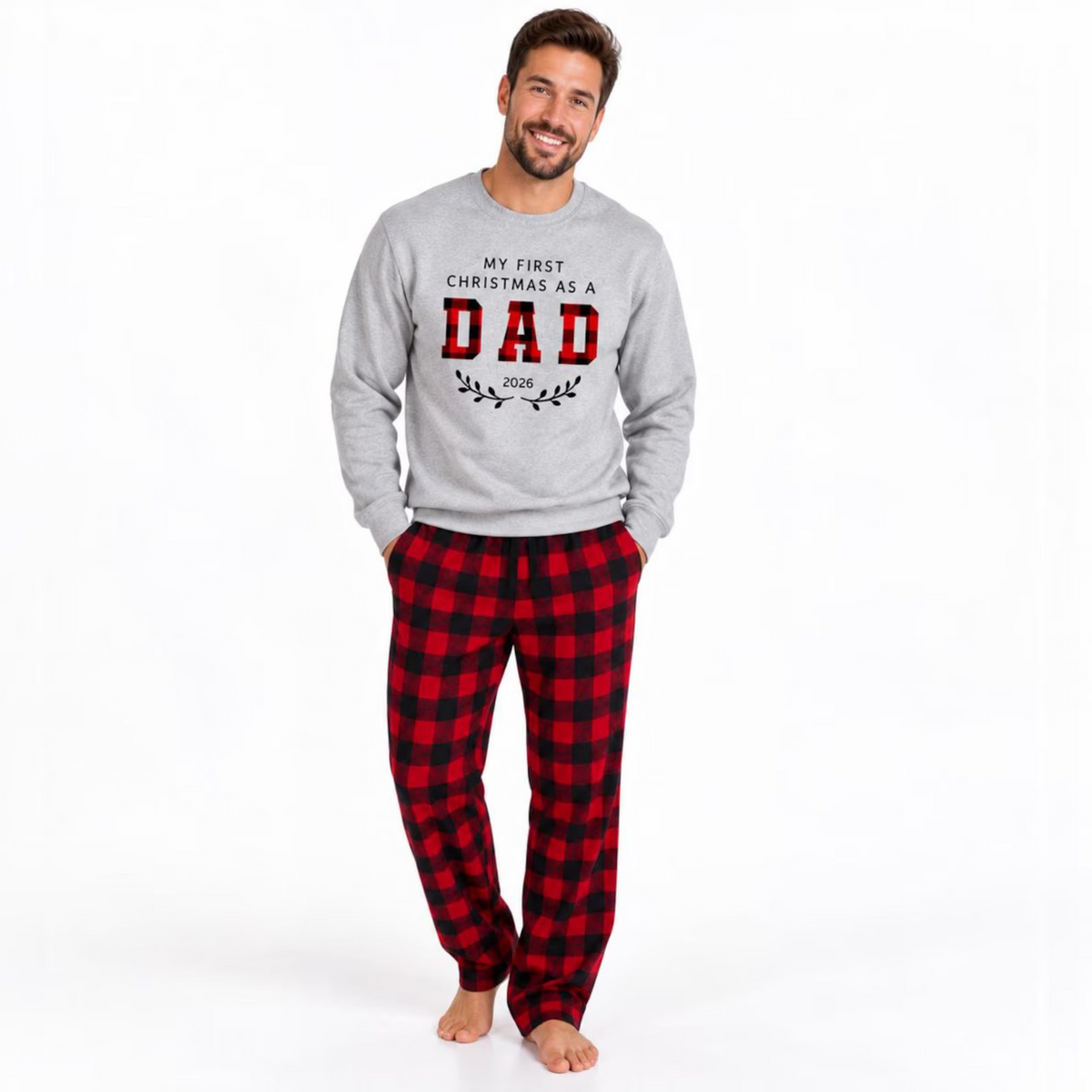 Man wearing a personalized First Christmas as Dad 2026 sweatshirt with red and black buffalo plaid pajama pants, posing in a clean studio setting.