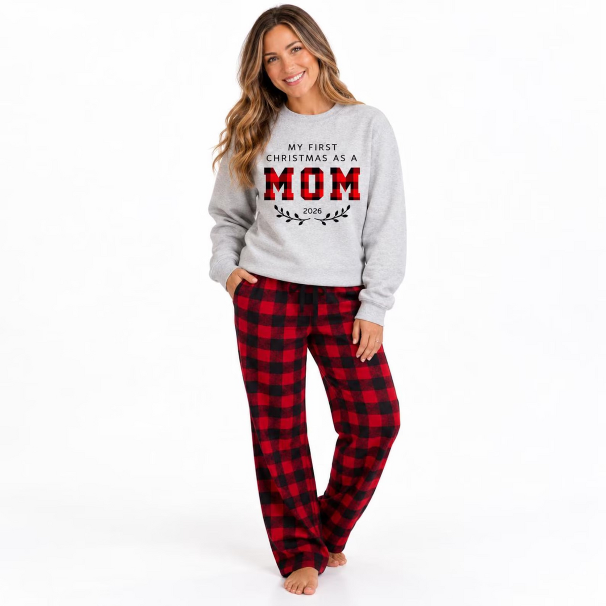Woman wearing a personalized First Christmas as Mom 2026 sweatshirt with red and black buffalo plaid pajama pants, posing in a clean studio setting.