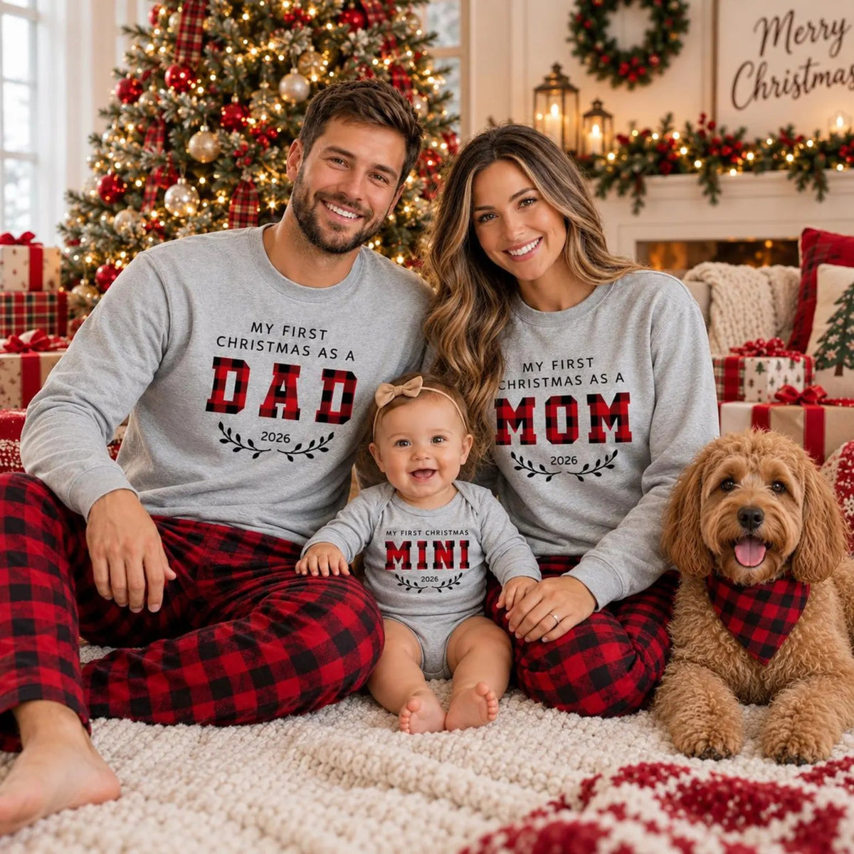 Family wearing matching First Christmas as Mom, Dad, and Mini 2026 sweatshirts with red and black buffalo plaid pajama pants, sitting together with their baby and dog in a cozy Christmas living room.