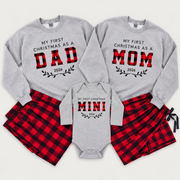 Matching First Christmas as Mom, Dad, and Mini family outfits featuring personalized 2026 sweatshirts, a baby bodysuit, and matching red and black buffalo plaid pajama pants.