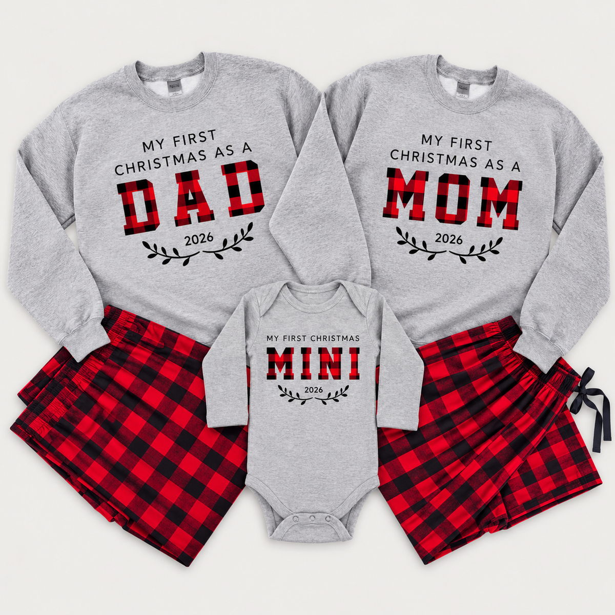 Matching First Christmas as Mom, Dad, and Mini family outfits featuring personalized 2026 sweatshirts, a baby bodysuit, and matching red and black buffalo plaid pajama pants.