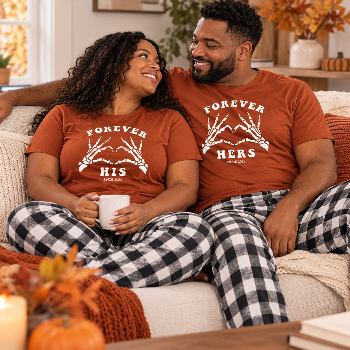 Couple wearing matching autumn Forever His and Forever Hers T-shirts with black and white flannel pajama pants, relaxing together on a cozy sofa