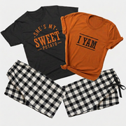 Flat lay of matching Thanksgiving pajamas featuring a black She's My Sweet Potato T-shirt, an autumn I Yam T-shirt, and white-and-black plaid flannel pajama pants 