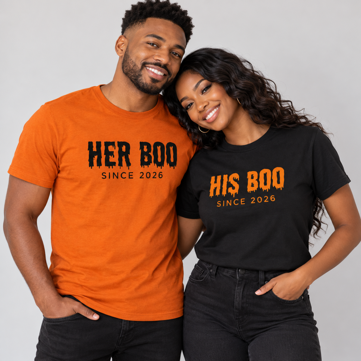 Couple wearing matching Her Boo and His Boo Halloween t-shirts, autumn for him and black for her, in a light gray studio