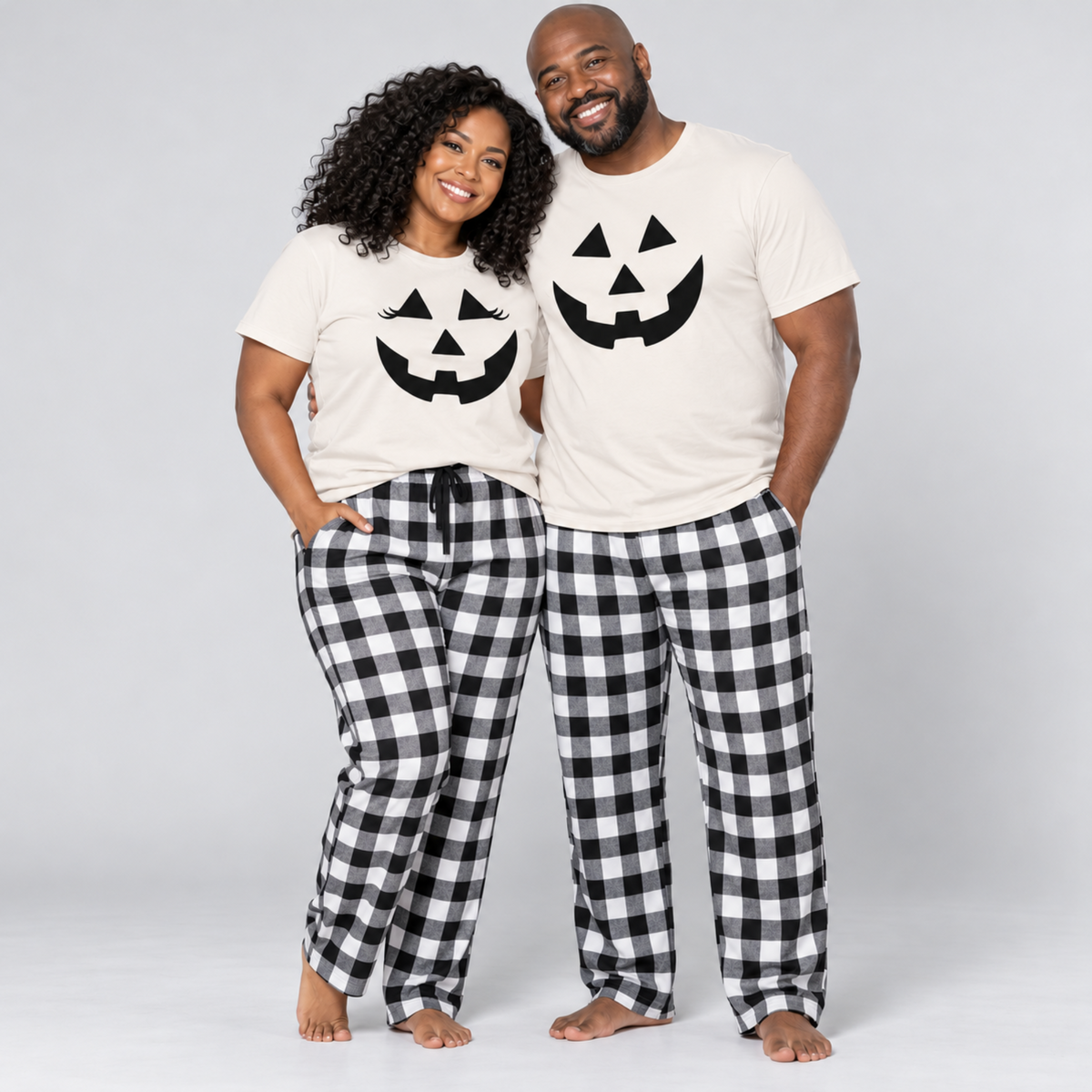 Couple wearing matching light color pumpkin Halloween t-shirts with black and white checkered flannel pajama pants in a light gray studio