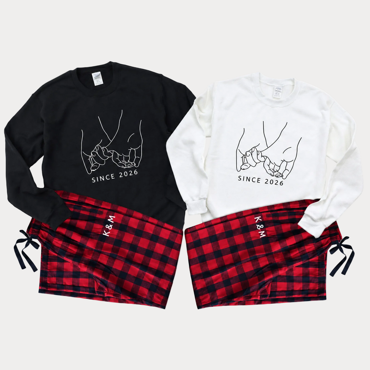 Matching couple pajama sets featuring black and white sweatshirts with a linked pinky illustration and “Since 2026” text, paired with red and black plaid pajama pants personalized with initials.