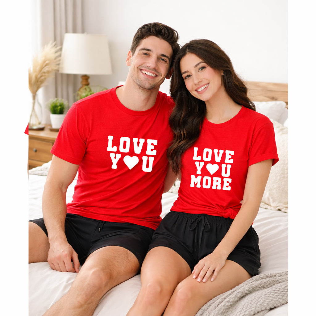 Couple sitting on a bed wearing matching “Love You” and “Love You More” pajama set in a cozy bedroom setting