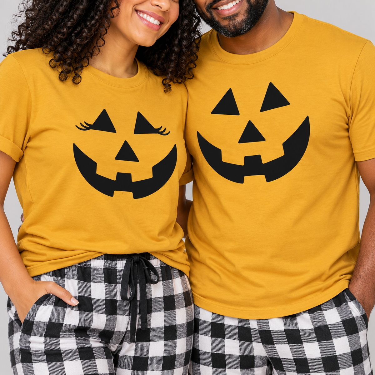 Couple wearing matching mustard pumpkin Halloween t-shirts with black and white checkered flannel pajama pants in a close-up studio setting