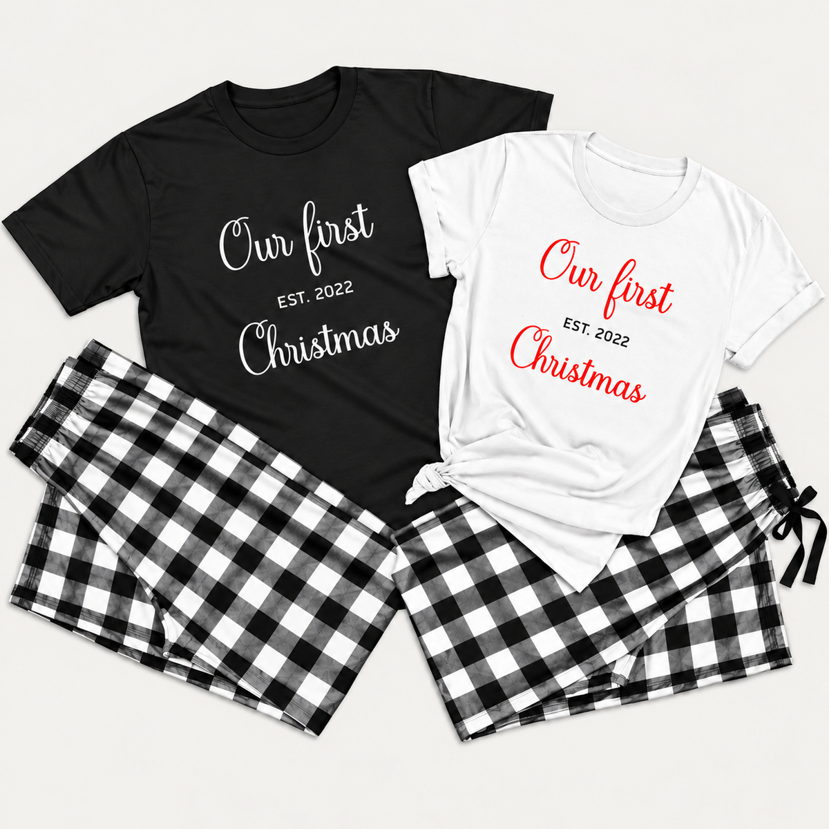 Matching Christmas pajamas featuring black and white T-shirts printed with “Our First Christmas” and “EST. 2022,” paired with black and white buffalo plaid flannel pajama bottoms in a clean studio flat lay.