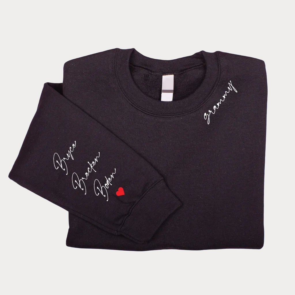 Black personalized Grandma sweatshirt featuring white script lettering on the chest and custom grandkids' names with a red heart on the sleeve.