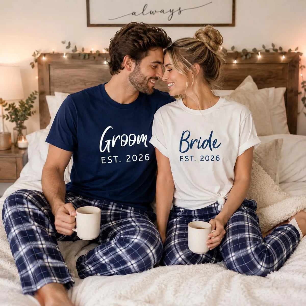 Couple holding mugs on a bed, wearing navy blue Groom and white Bride T-shirts with matching Navy-Silver plaid pajama pants.