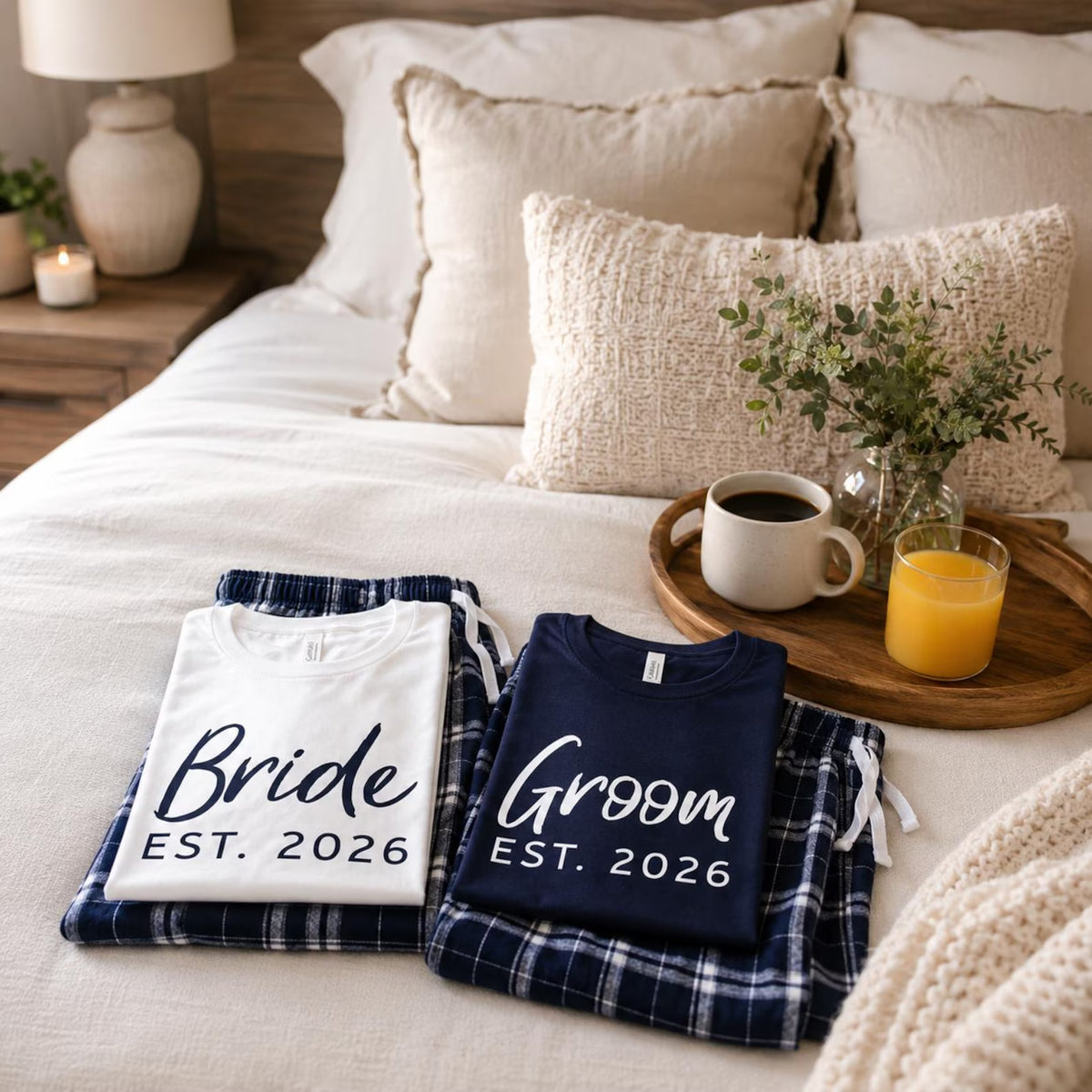 White Bride and navy blue Groom T-shirts with Navy-Silver plaid pajama pants, folded on a bed beside a breakfast tray.