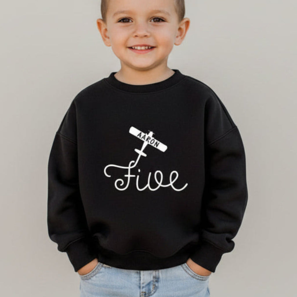 Boy model wearing black personalized 5th birthday airplane sweatshirt with custom name on white background