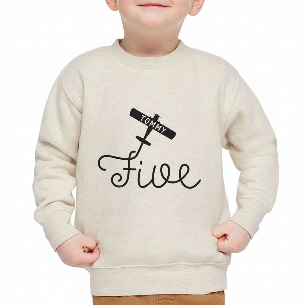 Boy model wearing a natural-color personalized 5th birthday airplane sweatshirt with custom name on white background