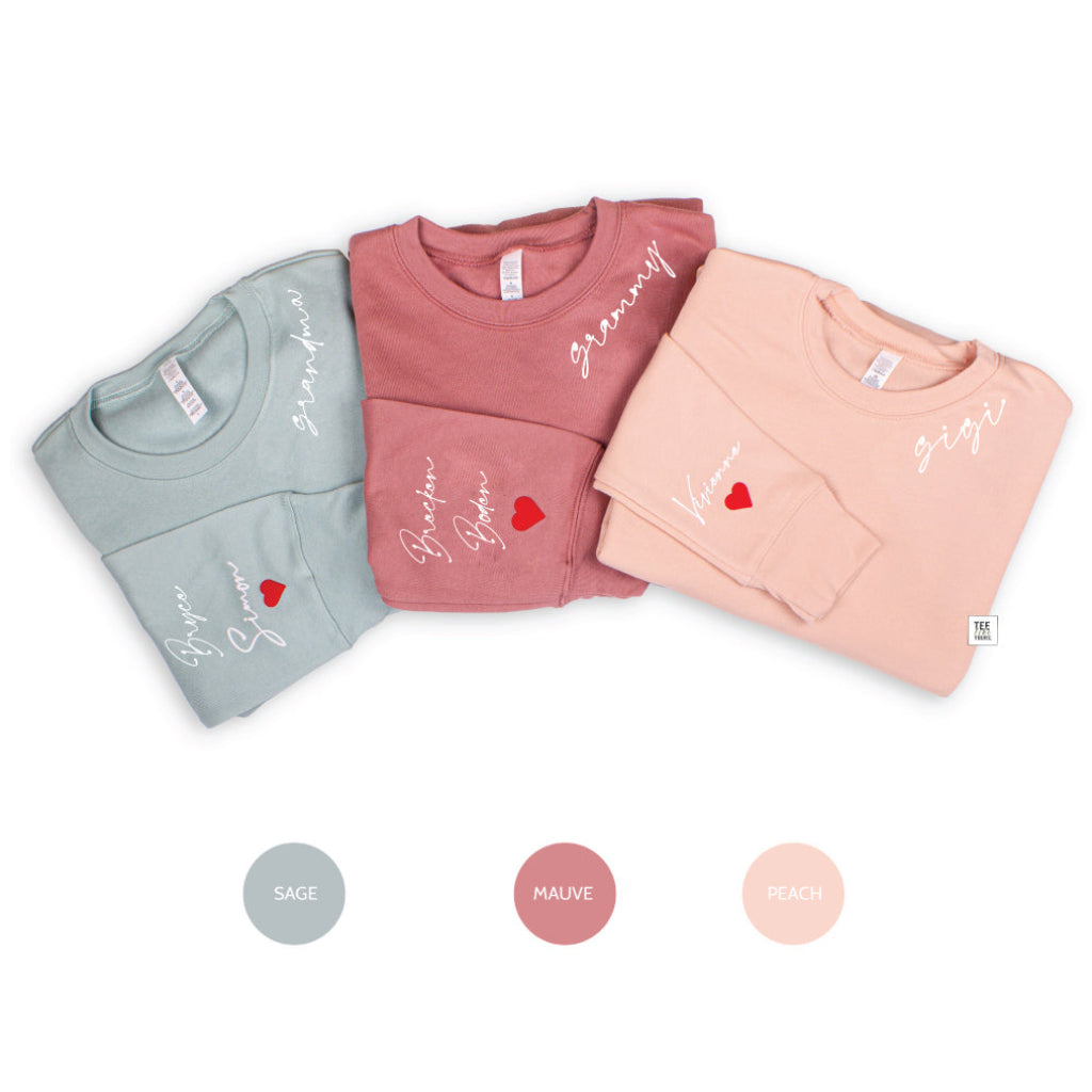 Three personalized Grandma sweatshirts in Sage, Mauve, and Peach, featuring custom script lettering close to the crew neck and grandkids' names with red hearts on the sleeves.