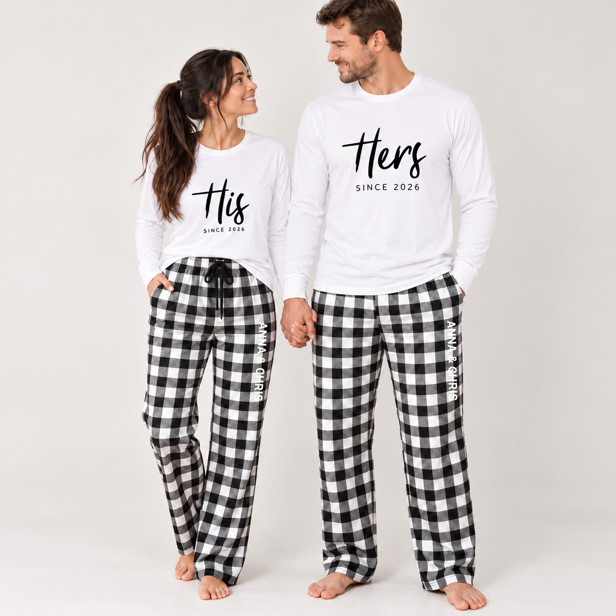 Couple wearing matching white long-sleeve His and Hers shirts with custom year prints and personalized black-and-white buffalo plaid flannel pajama pants featuring their names.