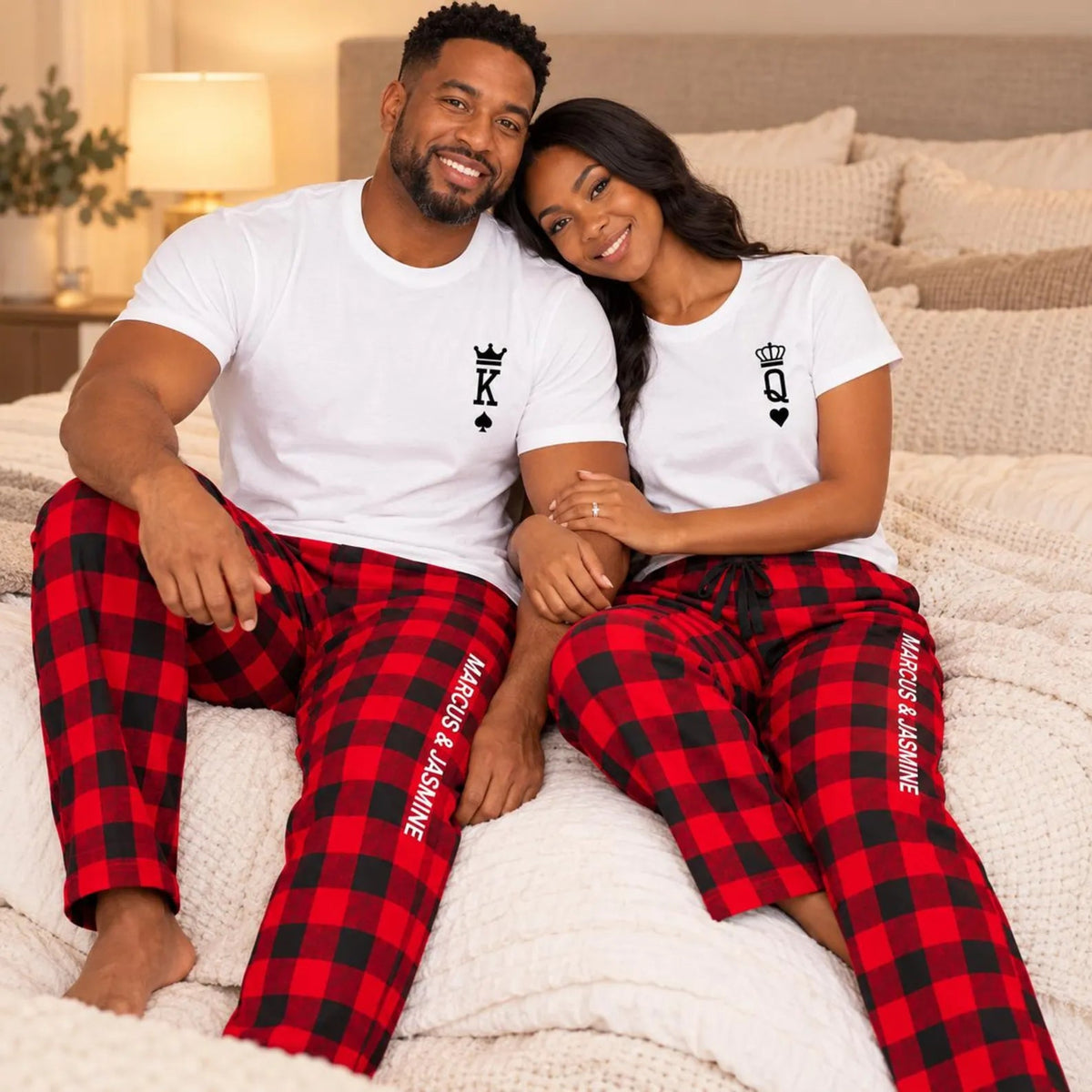 Couple wearing matching King and Queen T-shirts with personalized buffalo plaid flannel pajama pants featuring their custom names, sitting together on a cozy bed.