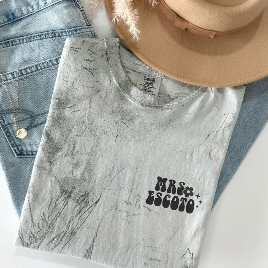 Personalized garment-dyed T-shirt with a Mrs. and custom name print on the front chest, styled with denim jeans and a hat.