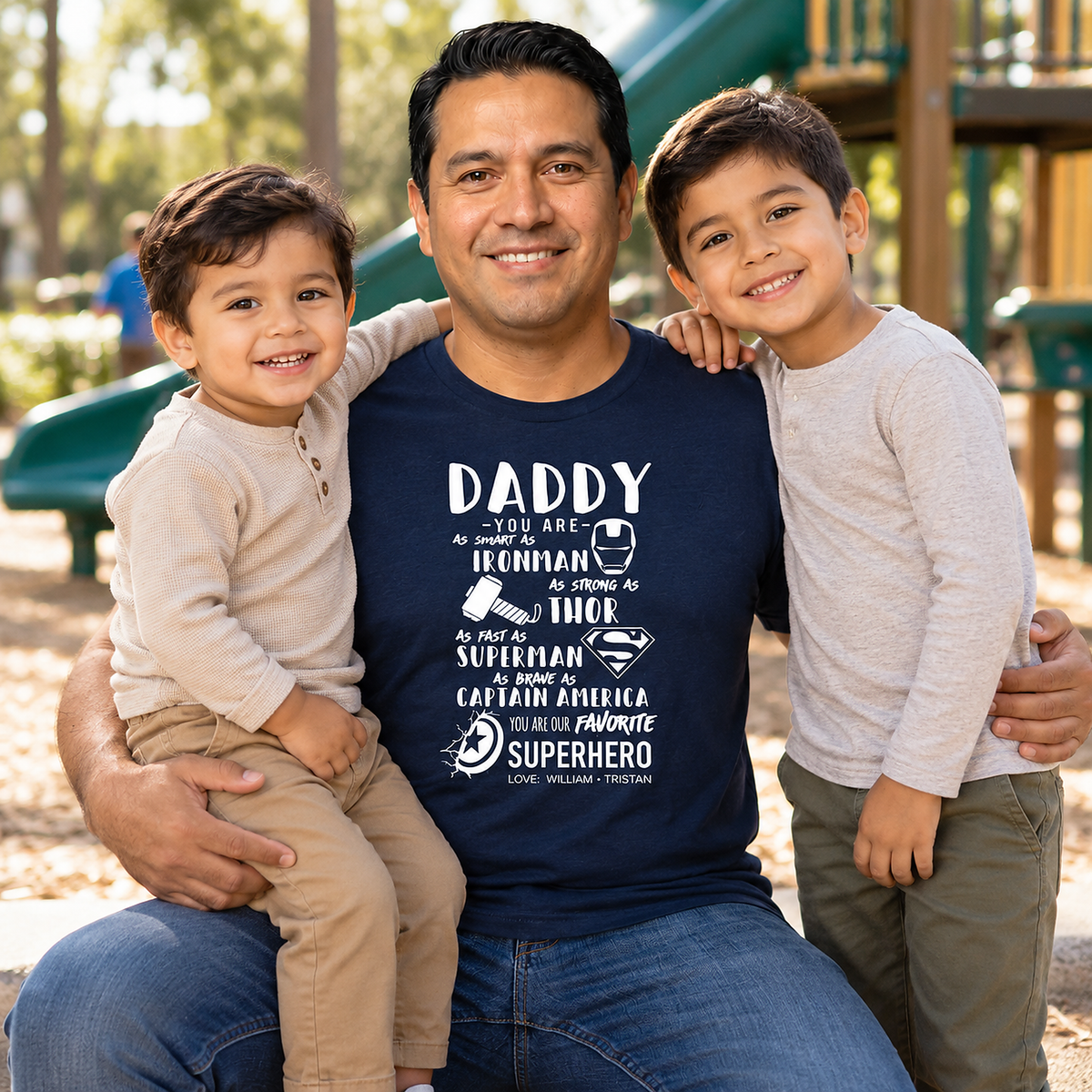 Father wearing a navy blue Bella + Canvas superhero Dad T-shirt with his two young sons in neutral-colored outfits at an outdoor playground.