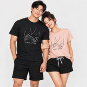Young couple wearing matching pinky promise graphic T-shirts and lounge shorts with personalized Since 2026 prints in a clean studio setting.