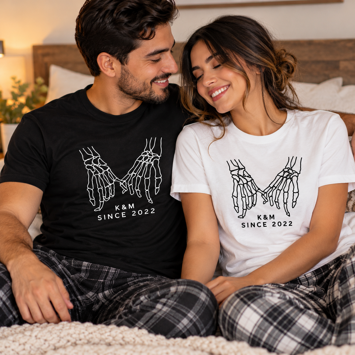 Couple wearing matching Pinkie Promise Halloween shirts, black for him and white for her, with skeleton hand designs in a cozy bedroom