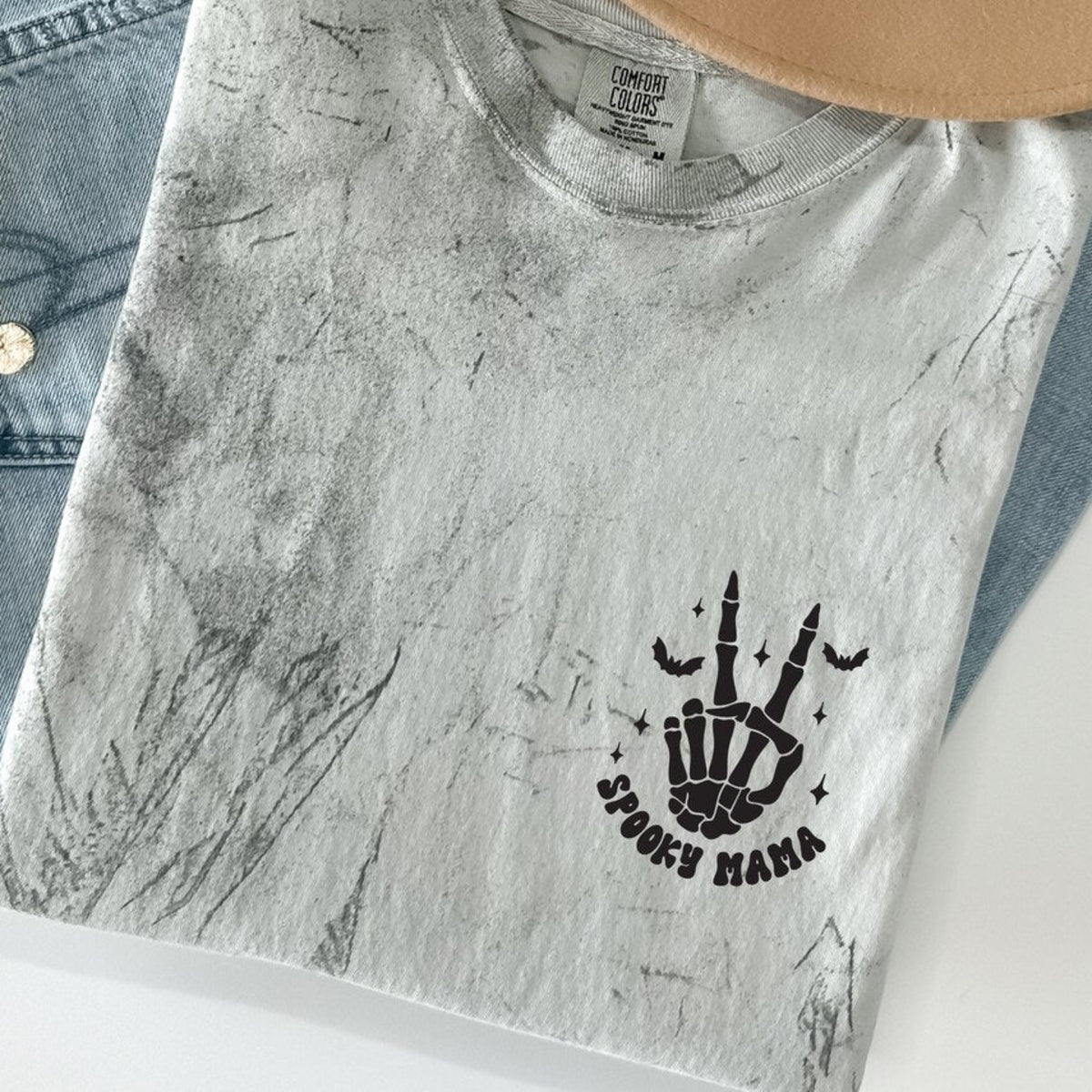 Folded Spooky Mama Halloween shirt featuring a black skeleton hand, bats, stars, and Spooky Mama graphic