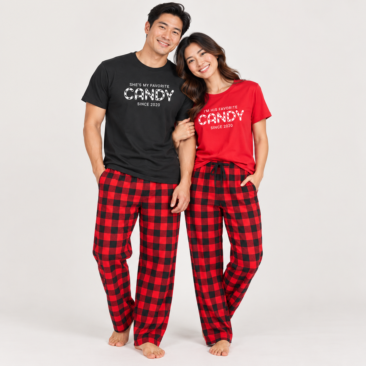Couple wearing matching favorite candy Christmas pajamas, with personalized black and red T-shirts and coordinating buffalo plaid flannel pajama pants.
