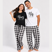 Couple wearing matching His and Hers pajamas featuring a black unisex T-shirt for the woman and a white unisex T-shirt for the man, personalized with established year designs, paired with black and white buffalo plaid flannel pajama pants. The woman's pajama pants feature black drawstring ties, while the man's pants have no visible ties.