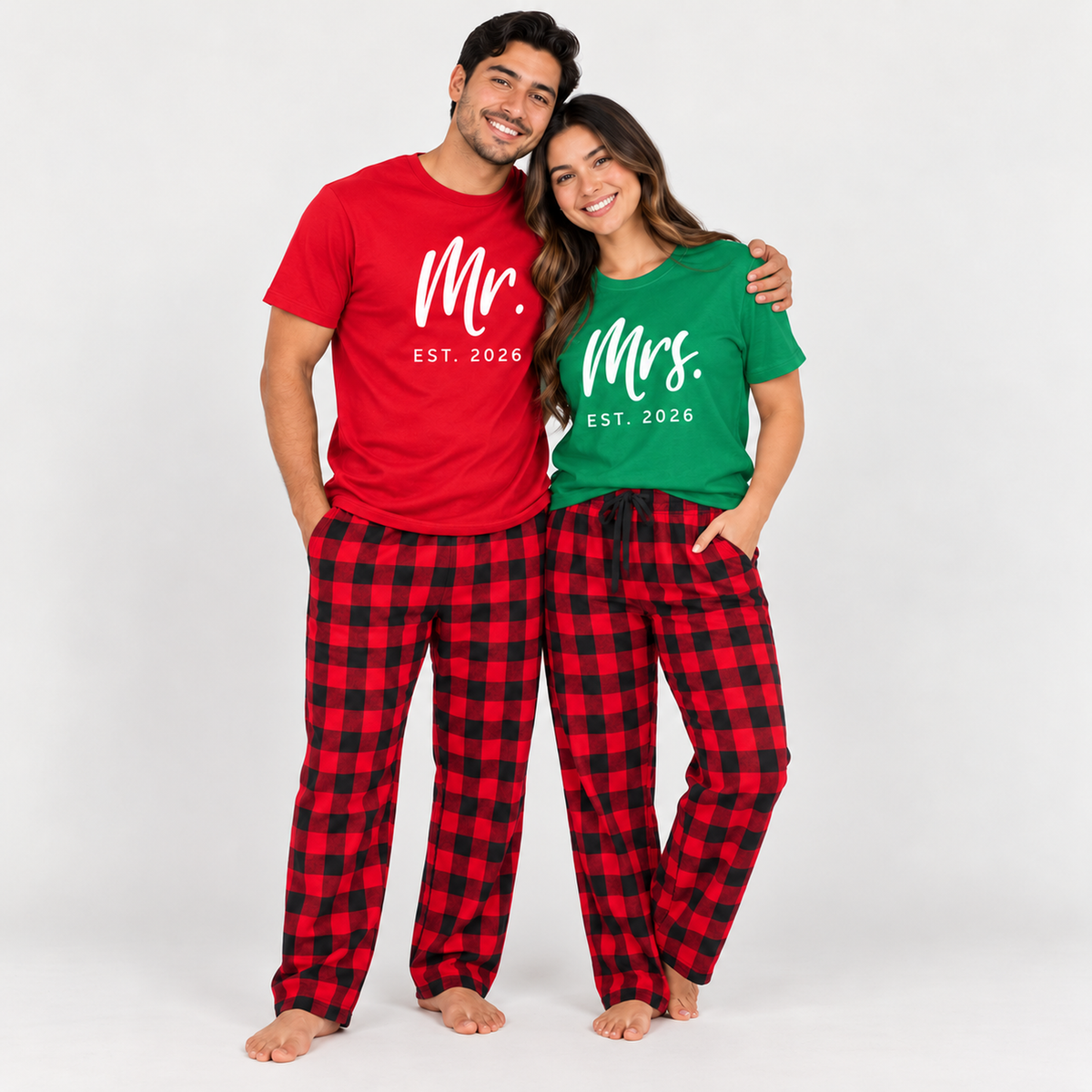 Smiling couple wearing matching red and Kelly green Mr. and Mrs. Est. 2026 T-shirts with red and black buffalo plaid flannel pajama pants.