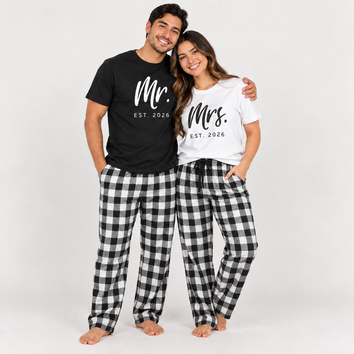 Smiling couple wearing matching white and black buffalo plaid pajama pants with Mr. and Mrs. Est. 2026 T-shirts for a wedding or anniversary celebration.