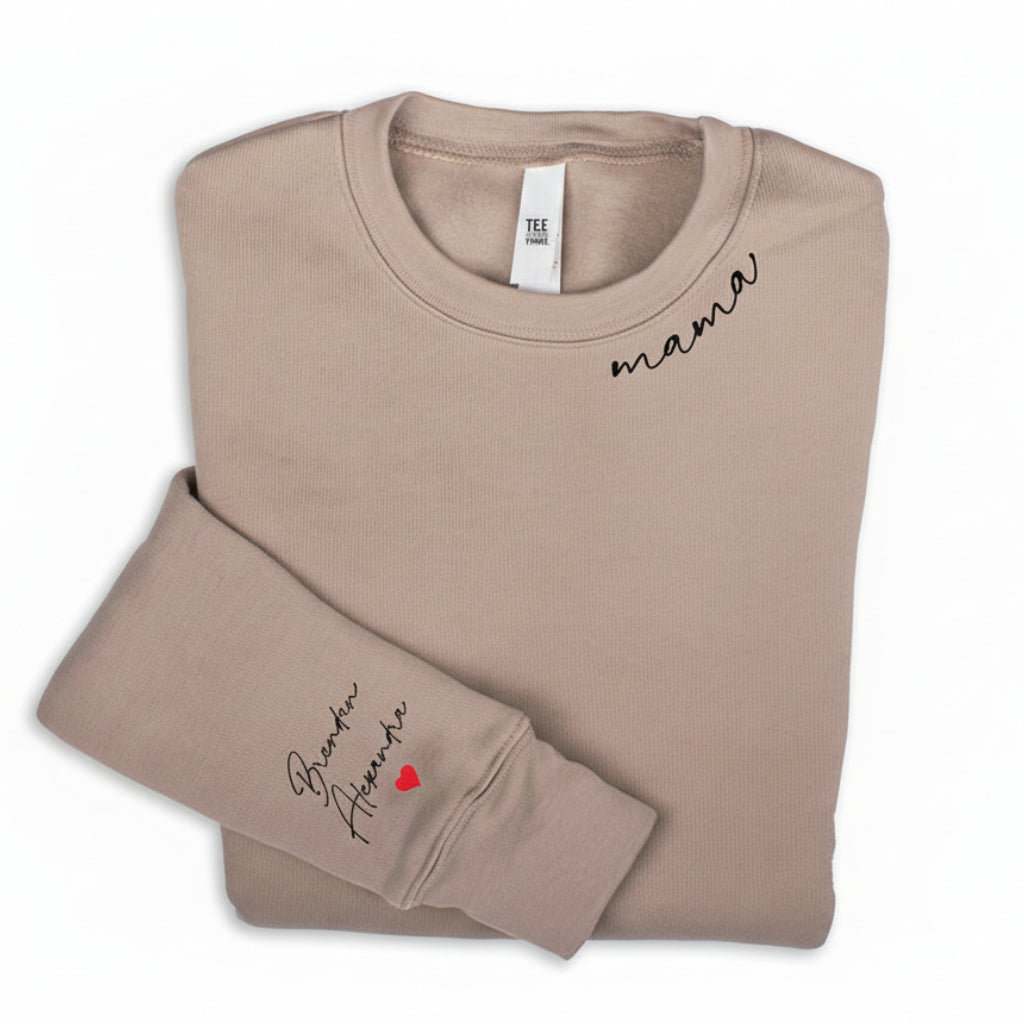 Folded beige sweatshirt with the word 'mama' written on the neckline and names on the right sleeve.