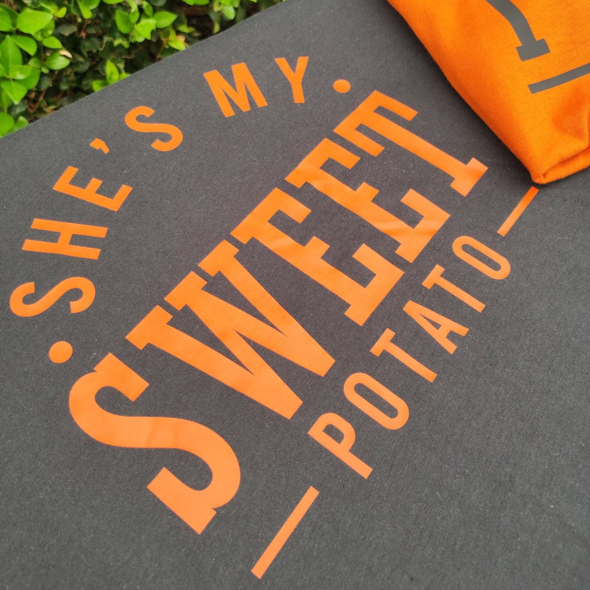 Close-up of the She's My Sweet Potato graphic printed on a black T-shirt, with a portion of an autumn T-shirt visible beside it.